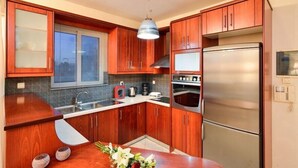 Una cocina compacta con armarios de madera, un refrigerador de acero inoxidable, un horno empotrado y un ventanal con persianas.
