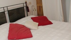 A bed with a white duvet and two red pillows, a wooden headboard, a bedside lamp, and a wooden wardrobe. - Guest house with a large terrace right by the pool (Murci)