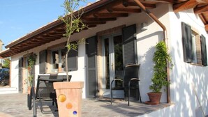 A house with a patio, a table, chairs, and a wooden planter. - Guest house with a large terrace right by the pool (Murci)