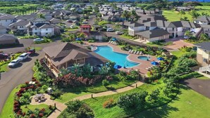 Una zona residencial con piscina rodeada de casas, un campo de golf al fondo y vistas despejadas al océano.