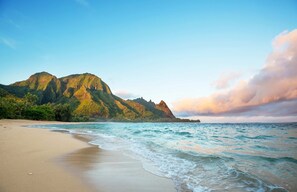 A beach with clear turquoise waters and a mountain in the background.