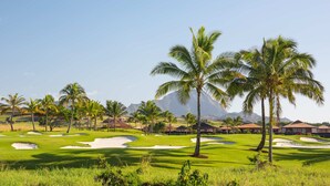 Un campo de golf con palmeras, búnkeres de arena y una montaña al fondo.