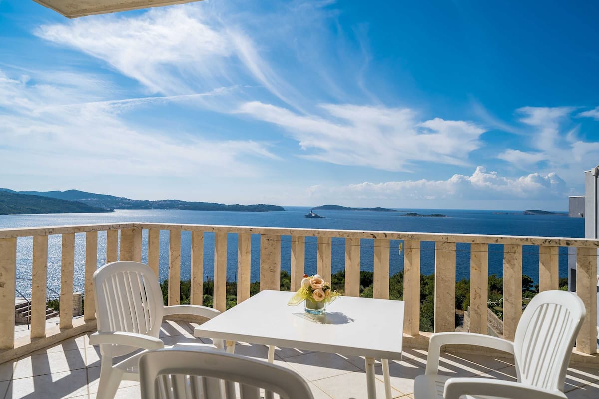 Ein Balkon mit Tisch und Stühlen, der auf ein Gewässer und ferne Inseln blickt.
