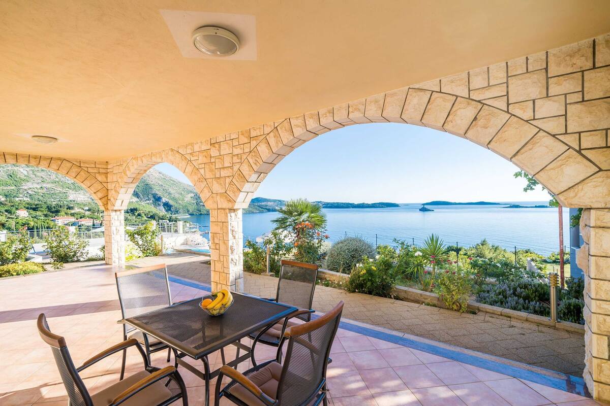 Eine Außenpatio mit Tisch und Stühlen, Steinbögen und Blick auf das Meer.