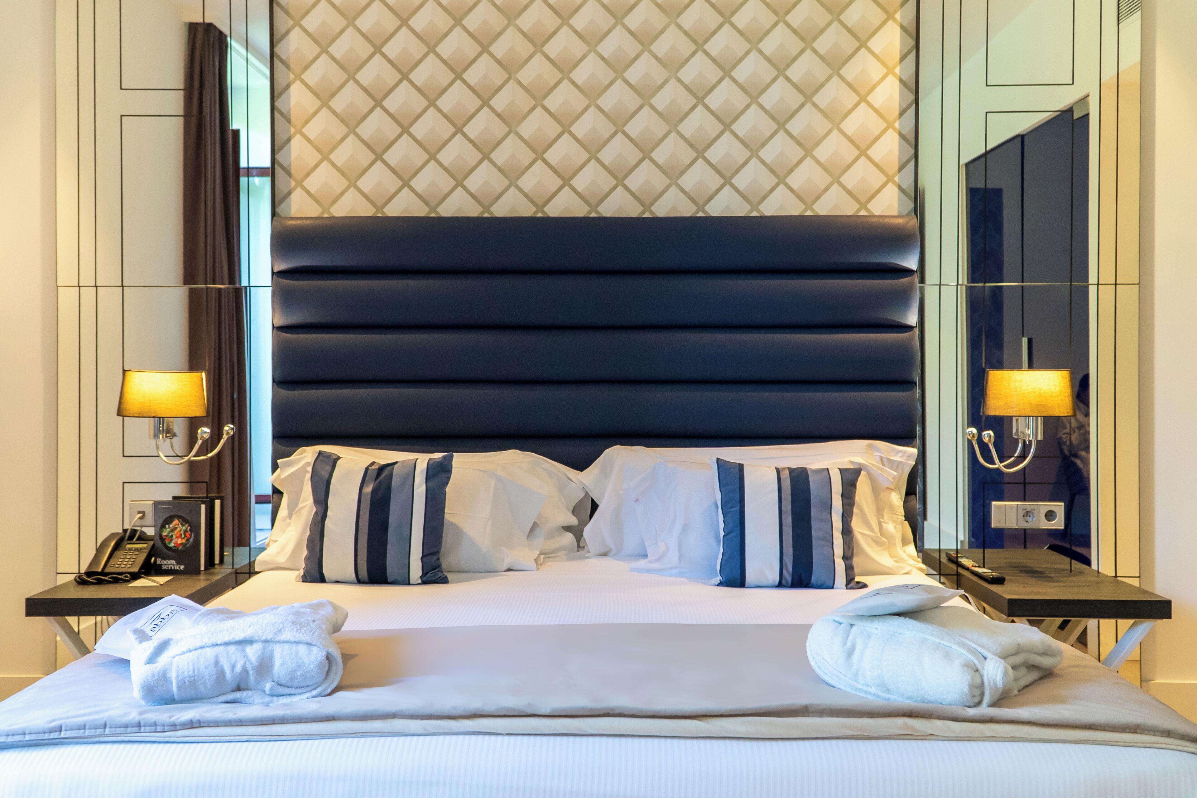 A hotel room with a large bed, two bedside tables, a nightstand, a telephone, and a lamp.