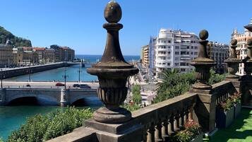 A balcony with a stone balustrade overlooking a cityscape with a river and buildings.