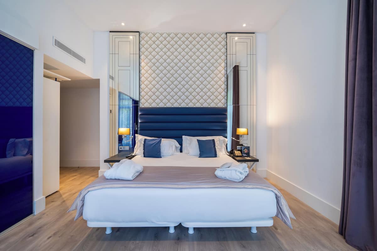 A modern hotel room with a large bed, a headboard with a geometric pattern, and a mirror on the wall.