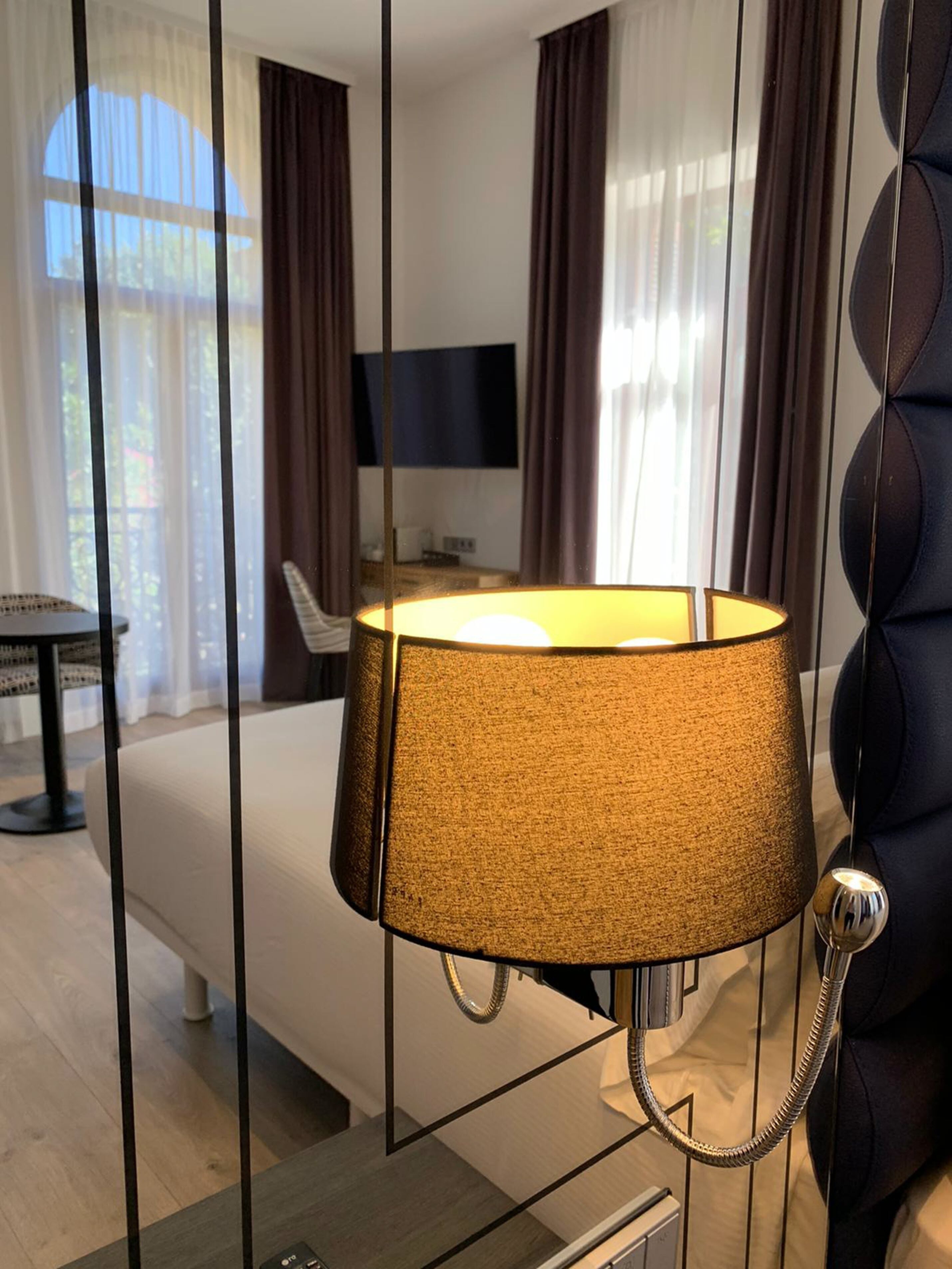 A modern hotel room with a bed, a bedside table, a lamp, and a TV on the wall.