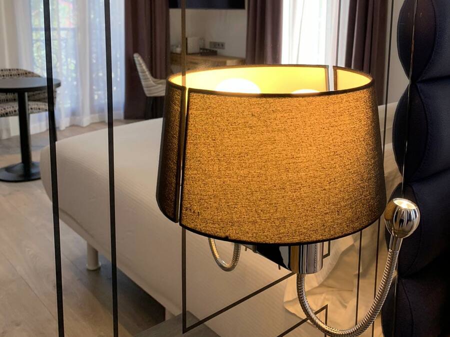 A modern hotel room with a bed, a bedside table, a lamp, and a TV on the wall.