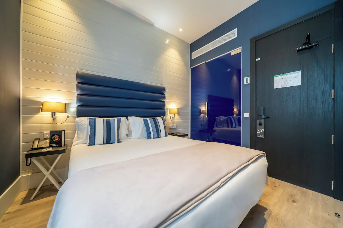 A modern hotel room with a large bed, bedside lamps, a nightstand, and a door with a sign.