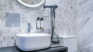 Et moderne badeværelse med et rundt spejl, en hvid vask, en hårtørrer og et toilet.