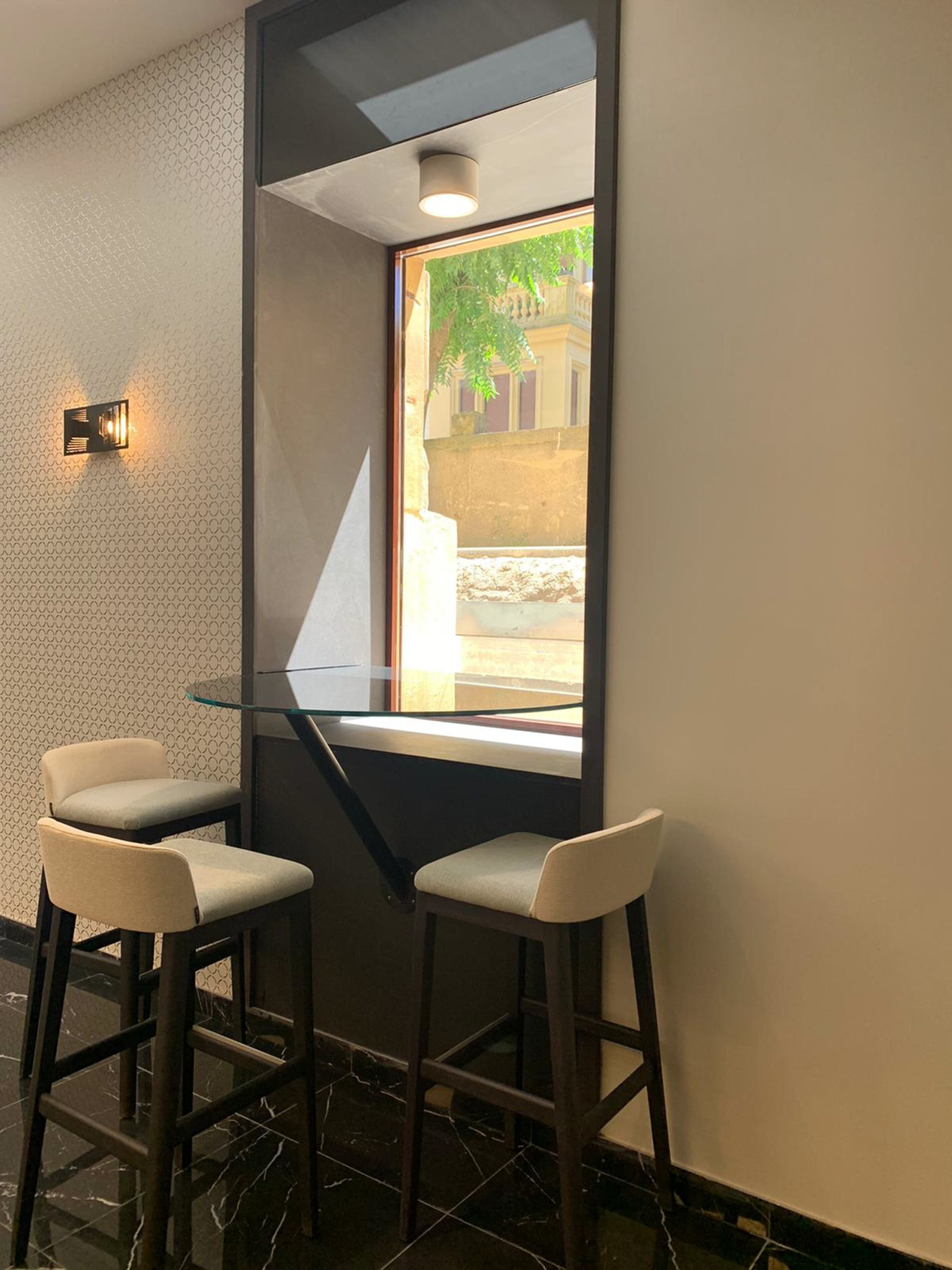Un bar en esquina con dos taburetes altos, un separador de vidrio y vista a la calle.
