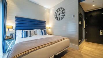A modern hotel room with a large bed, a wall clock, and a bedside table with a lamp.