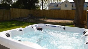 A hot tub in a backyard with a wooden fence and a house in the background. - Romney House (Hythe)
