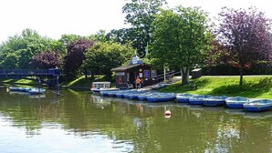 A lakeside dock with several small boats, a small cabin-like structure, and a bridge in the background. - Romney House (Hythe)