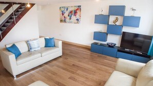A living room with a sofa, a TV, and a blue shelving unit. - Romney House (Hythe)