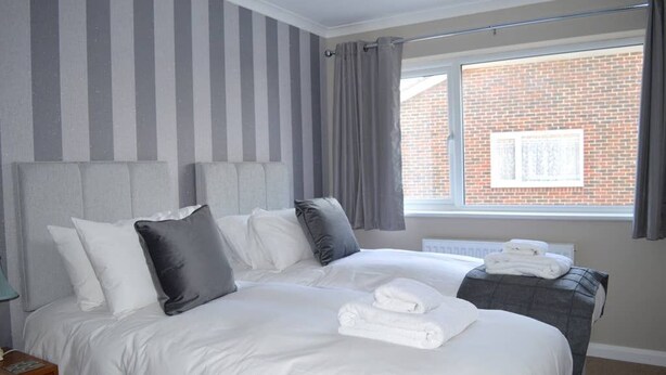 A hotel room with a large bed, a bedside table, a window with curtains, and a brick wall visible through the window. - Romney House (Hythe)