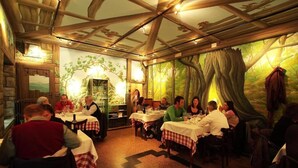 A restaurant with wooden beams and a forest mural on the wall. Tables are set with white tablecloths and red and white checkered table runners. - Locanda Amerigo dal 1934 (Valsamoggia)