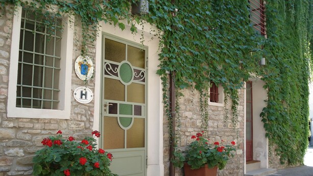 A stone building with a green door, two potted red flowers, and a window with a metal grill. - Locanda Amerigo dal 1934 (Valsamoggia)