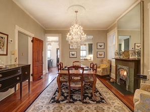 A dining room with a chandelier, wooden dining table, and chairs. There is a fireplace with decorative items and a rug on the floor. - Heated Pool Access | 5*Clean | Flex Cancelation (Savannah)