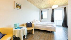Una habitación con cama, sofá, una mesita y ventana con cortinas.