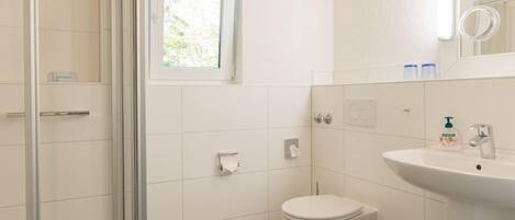 Un baño con cabina de ducha de vidrio, inodoro y lavamanos.