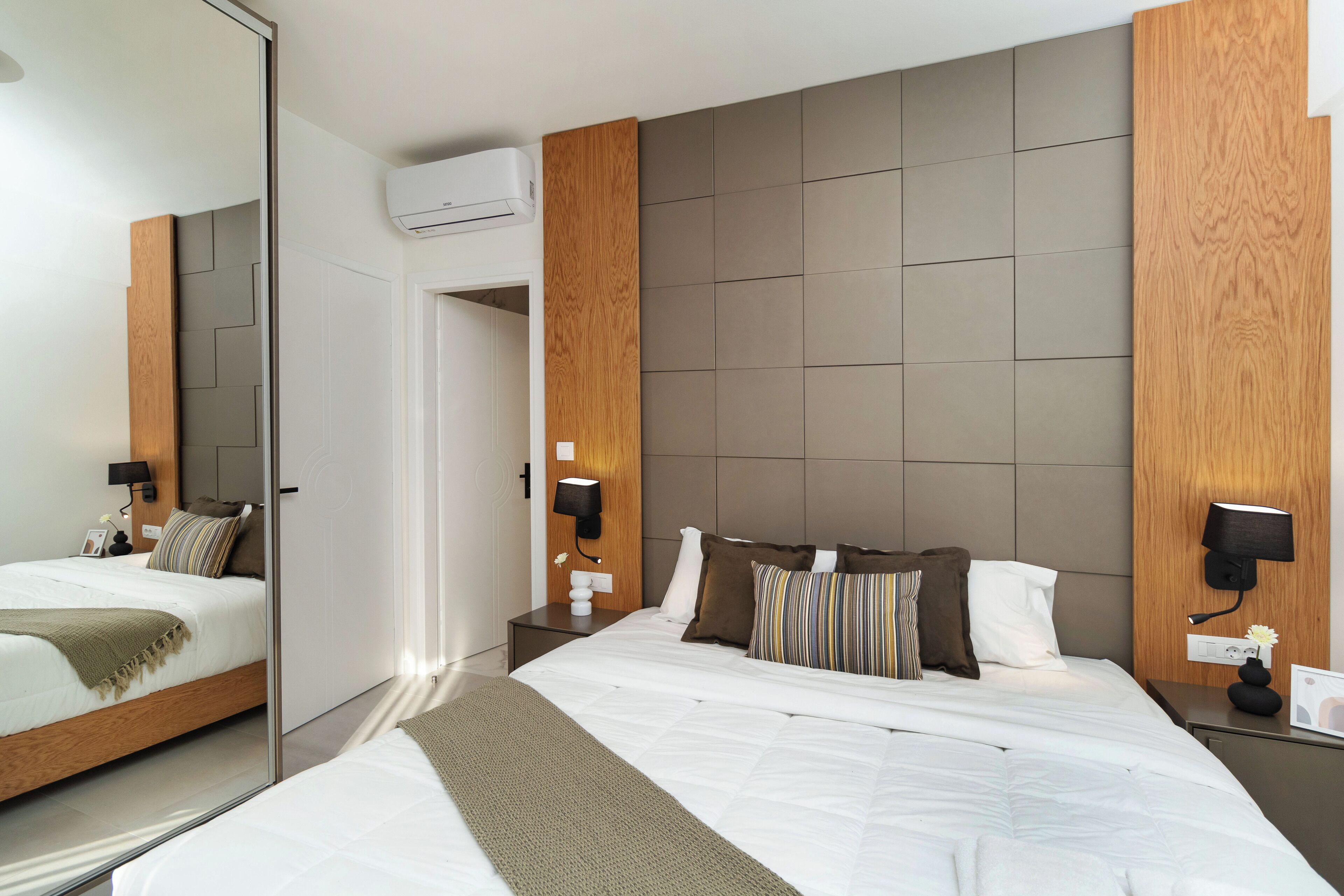 Een moderne hotelkamer met een groot bed, een houten hoofdeinde en een wandgemonteerde airconditioning.