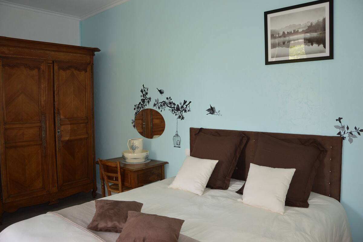 Un dormitorio con cama, un armario de madera, una mesita con lámpara y una pared decorada con un motivo natural.