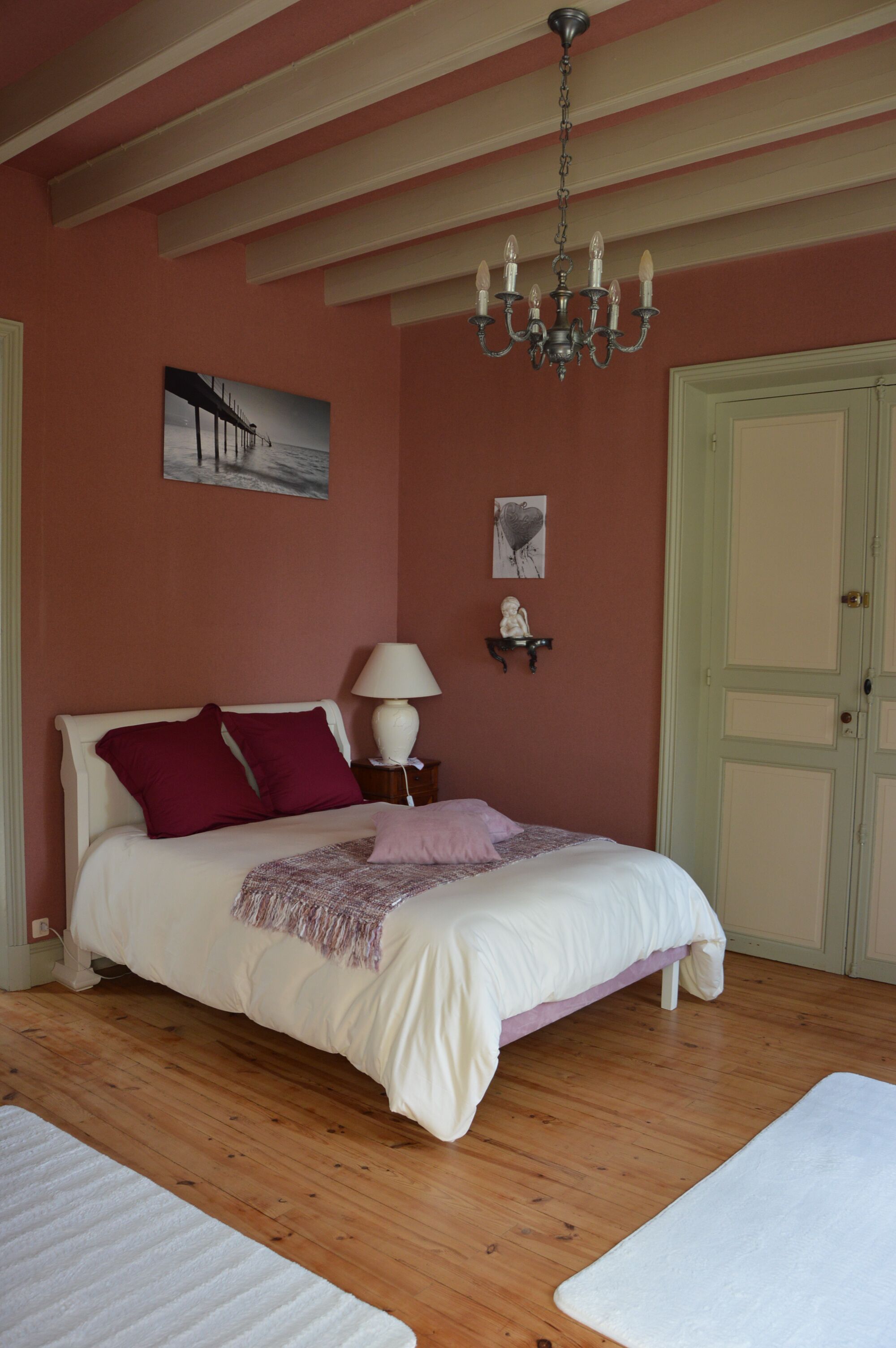 A bedroom with a bed, a chandelier, a nightstand, and a door.