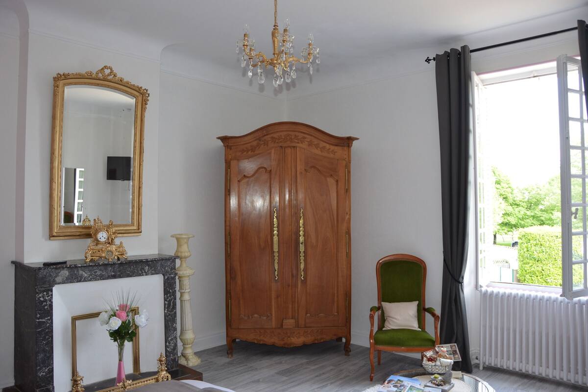Una habitación con un armario de madera, un espejo, una silla verde y una chimenea.
