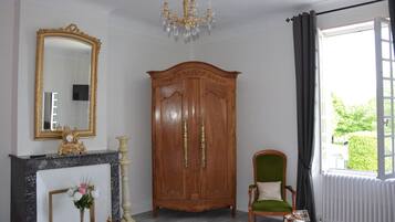 A room with a wooden wardrobe, a mirror, a green chair, and a fireplace.