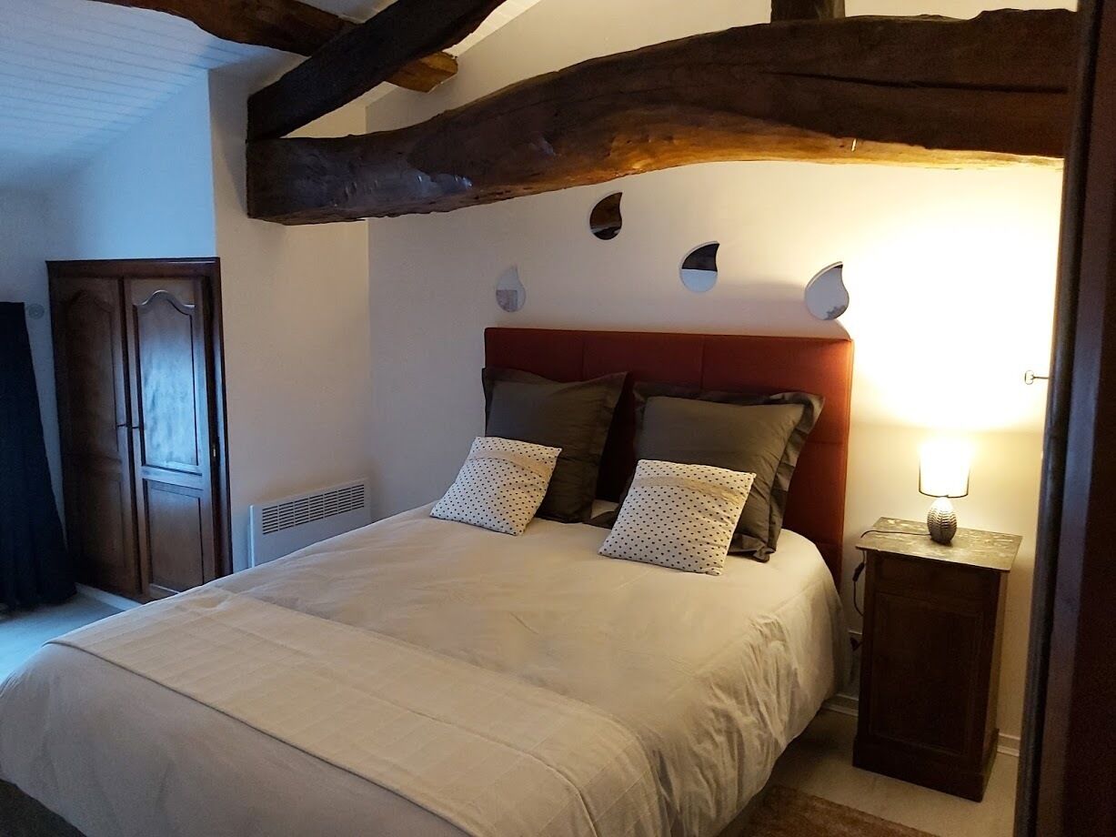 A bedroom with a bed, wooden headboard, two pillows, a bedside table with a lamp, and a wardrobe.