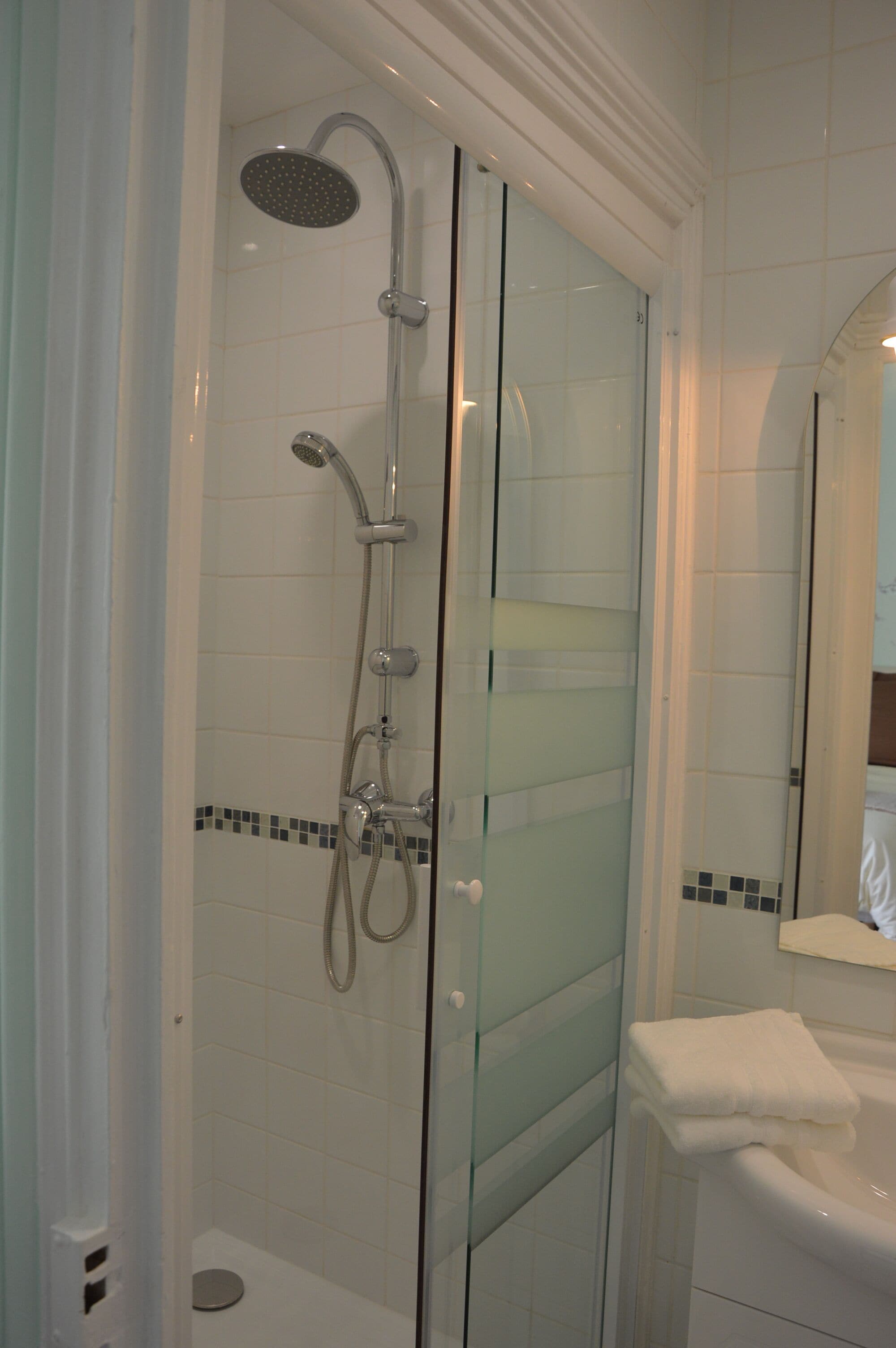 Une douche fermée par des parois en verre, dotée d’un pommeau de douche à main et d’un robinet fixé au mur.
