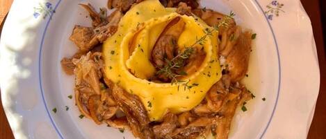 Ein Teller mit Fleisch und Kartoffelpüree, garniert mit Kräutern, auf einem Holztisch.