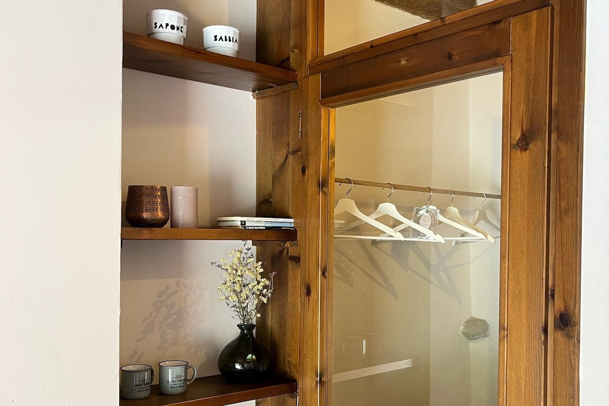 A wooden door with a frosted glass panel, wooden shelves with various items, and a hanging rack with clothes.