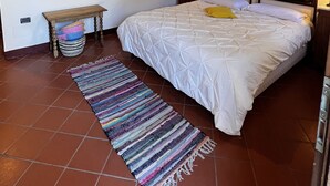 A bedroom with a large bed, a stone wall, wooden beams, a hanging light fixture, and a small table with a basket. - Agriturismo Rio Verde (Sasso Marconi)