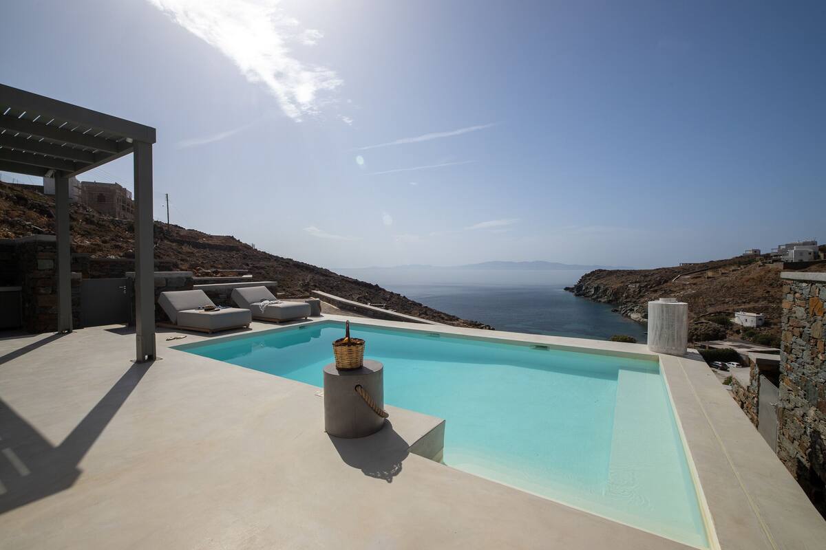 Une piscine avec vue sur la mer, des chaises longues et une pergola.