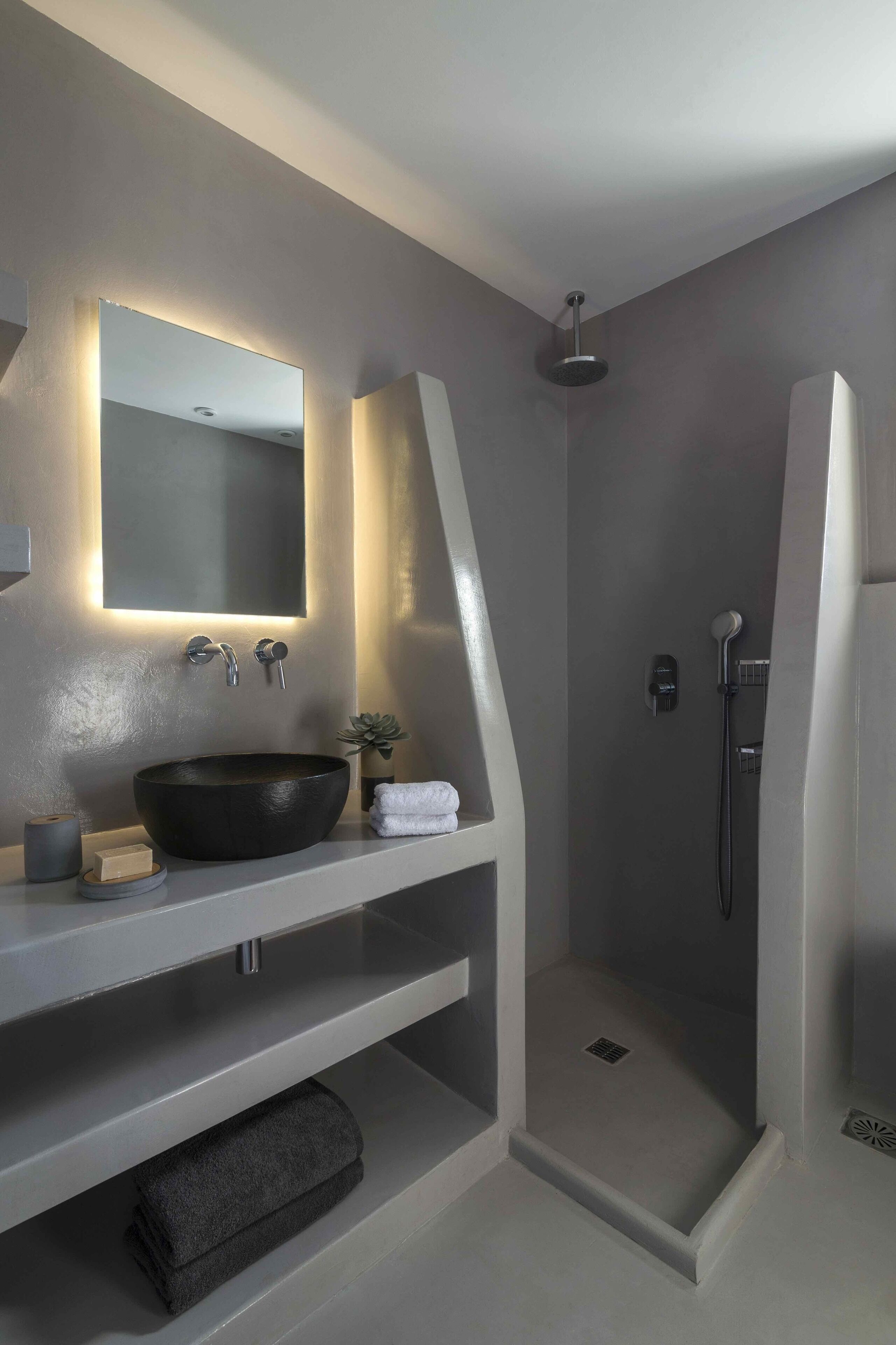 A modern bathroom with a large mirror, a round sink, and a walk-in shower.
