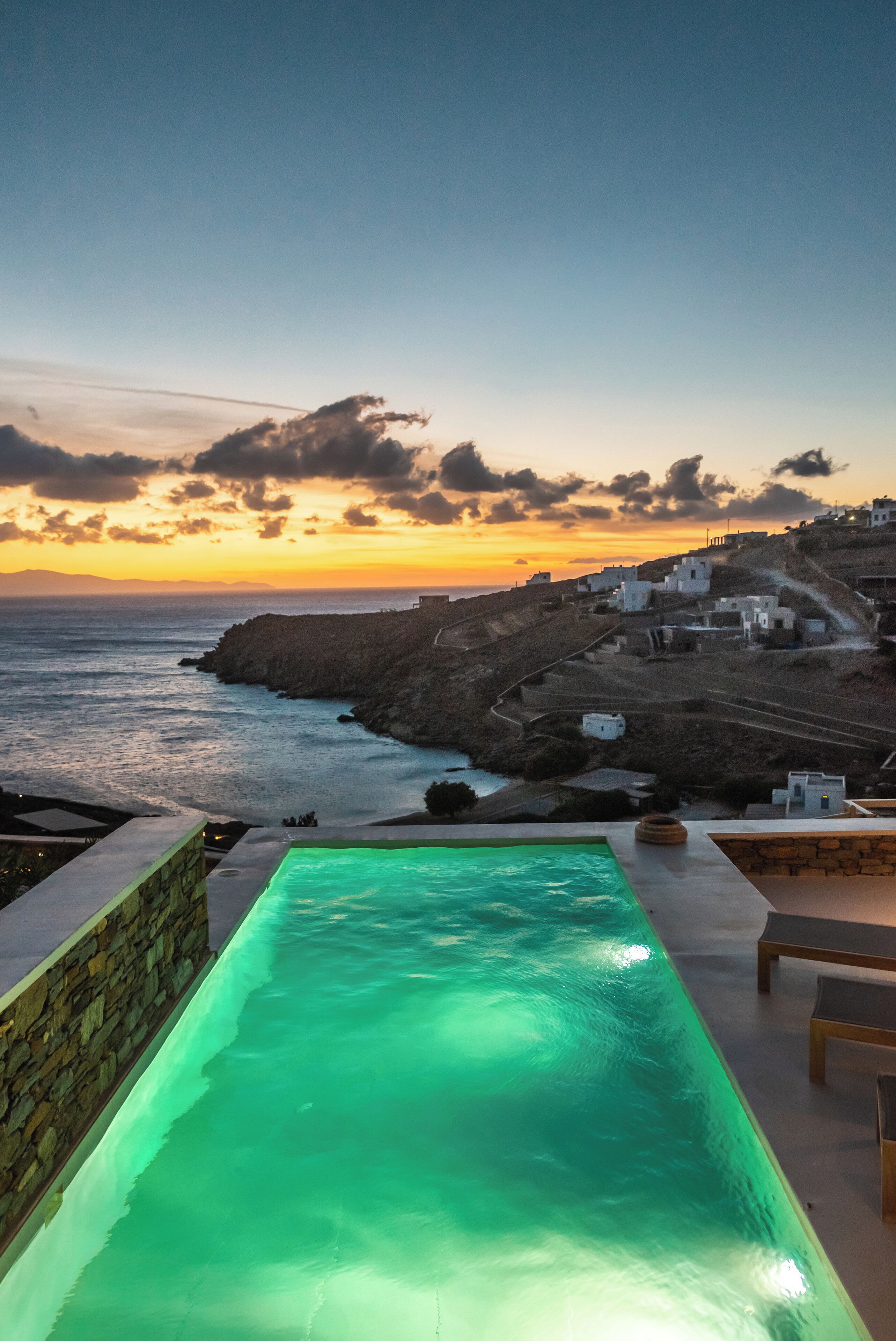 Ein Swimmingpool mit Blick auf das Meer und ein Küstendorf bei Sonnenuntergang.