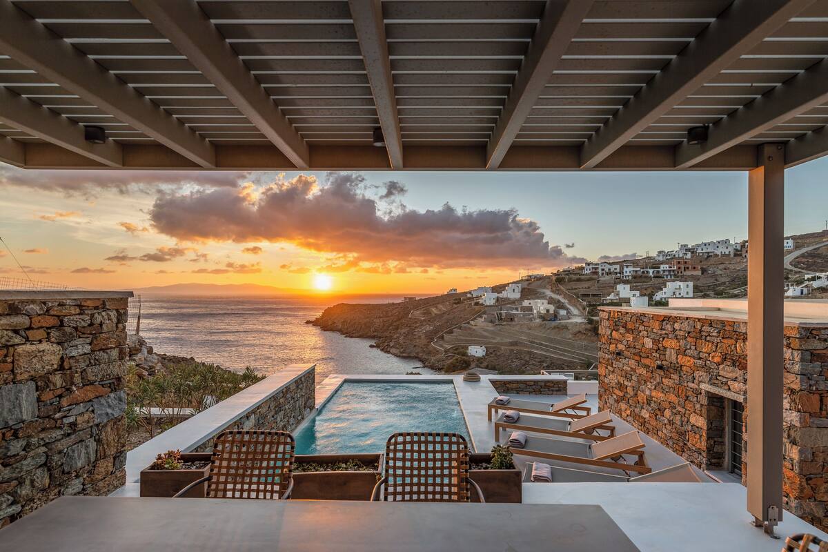 Une piscine sur le toit, dotée de chaises longues, un mur en pierre et une vue sur le coucher de soleil sur la mer.