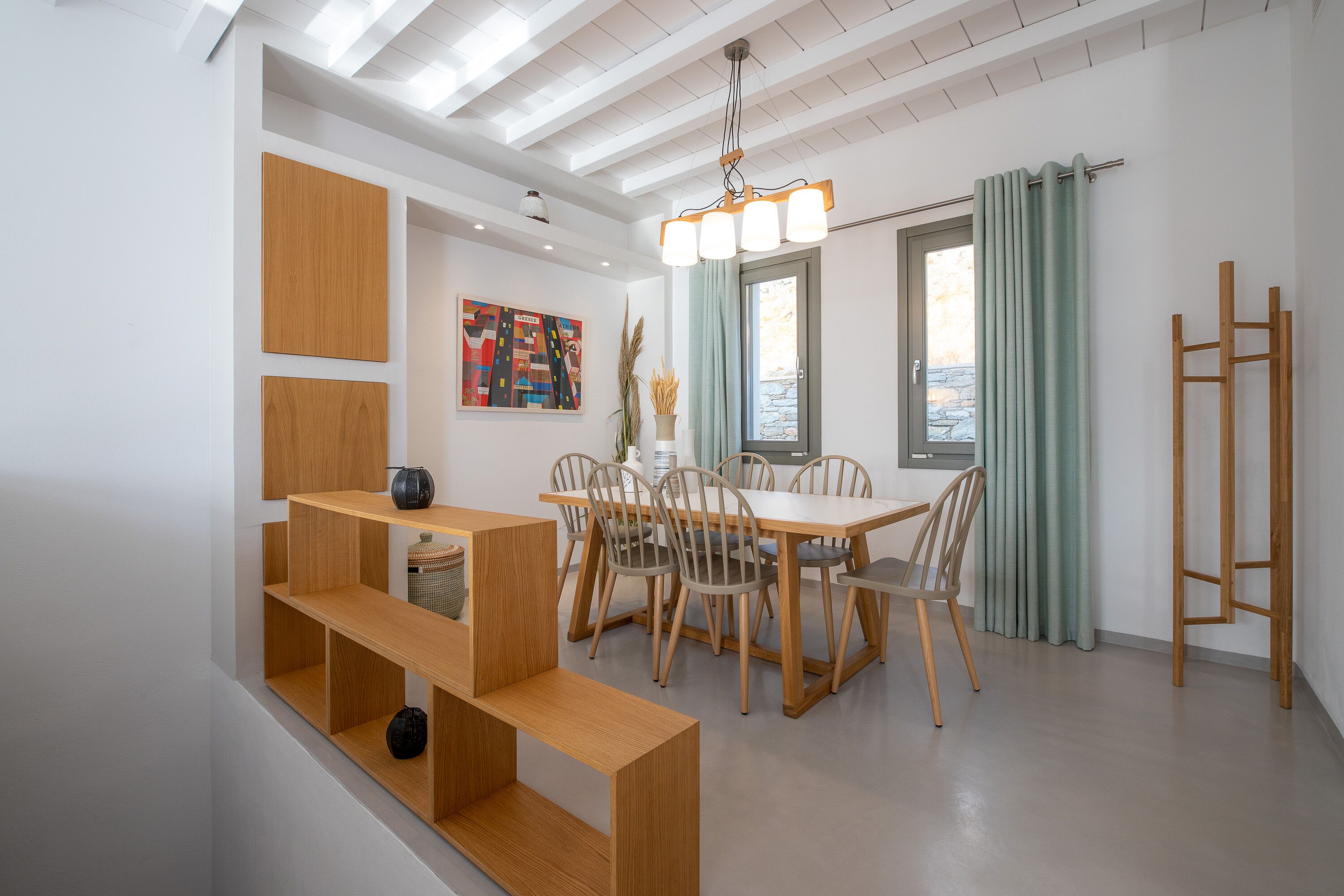 A modern dining area with a wooden table and chairs, a hanging light fixture, and a view of the outdoors through a window.