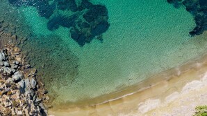 Vista aérea de uma praia com águas turquesa cristalinas, costa rochosa e áreas de areia.