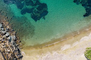 Vista aérea de una playa con agua turquesa cristalina, costa rocosa y zonas de arena.