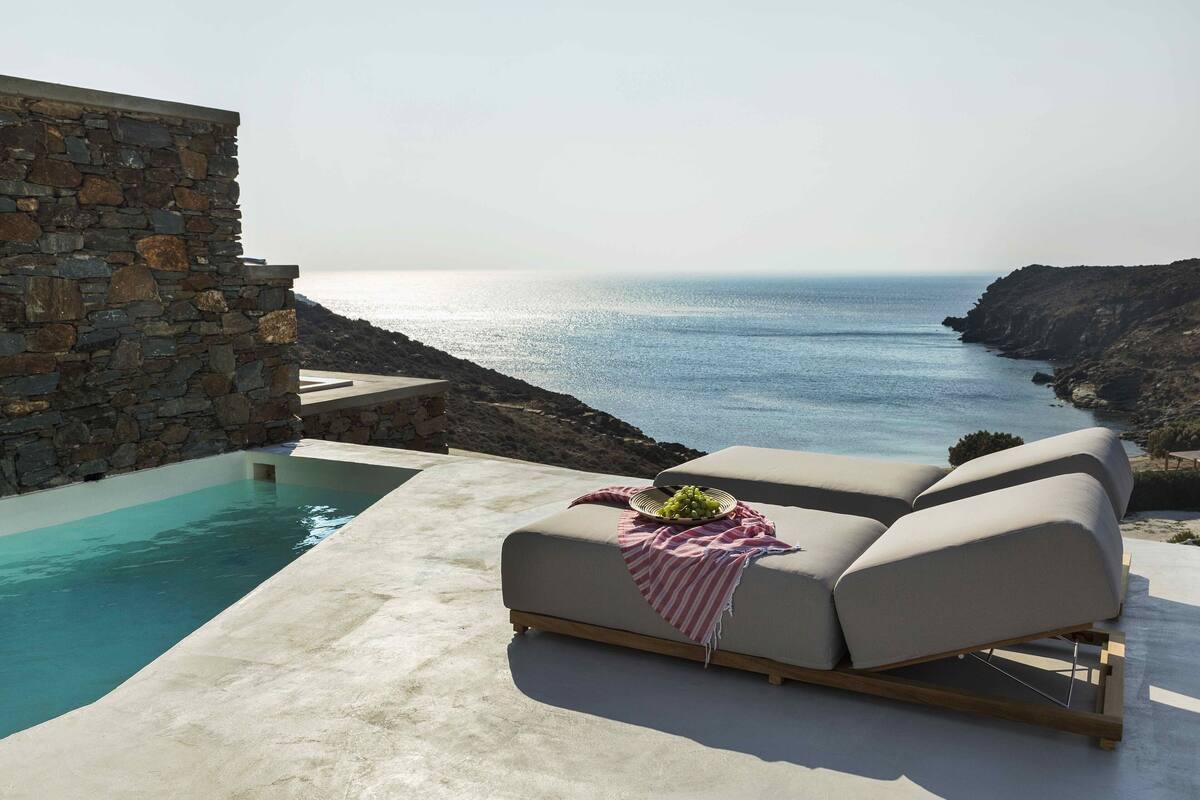Un espace aménagé au bord de la piscine, avec un mur en pierre, un fauteuil de relaxation et une vue sur la mer.