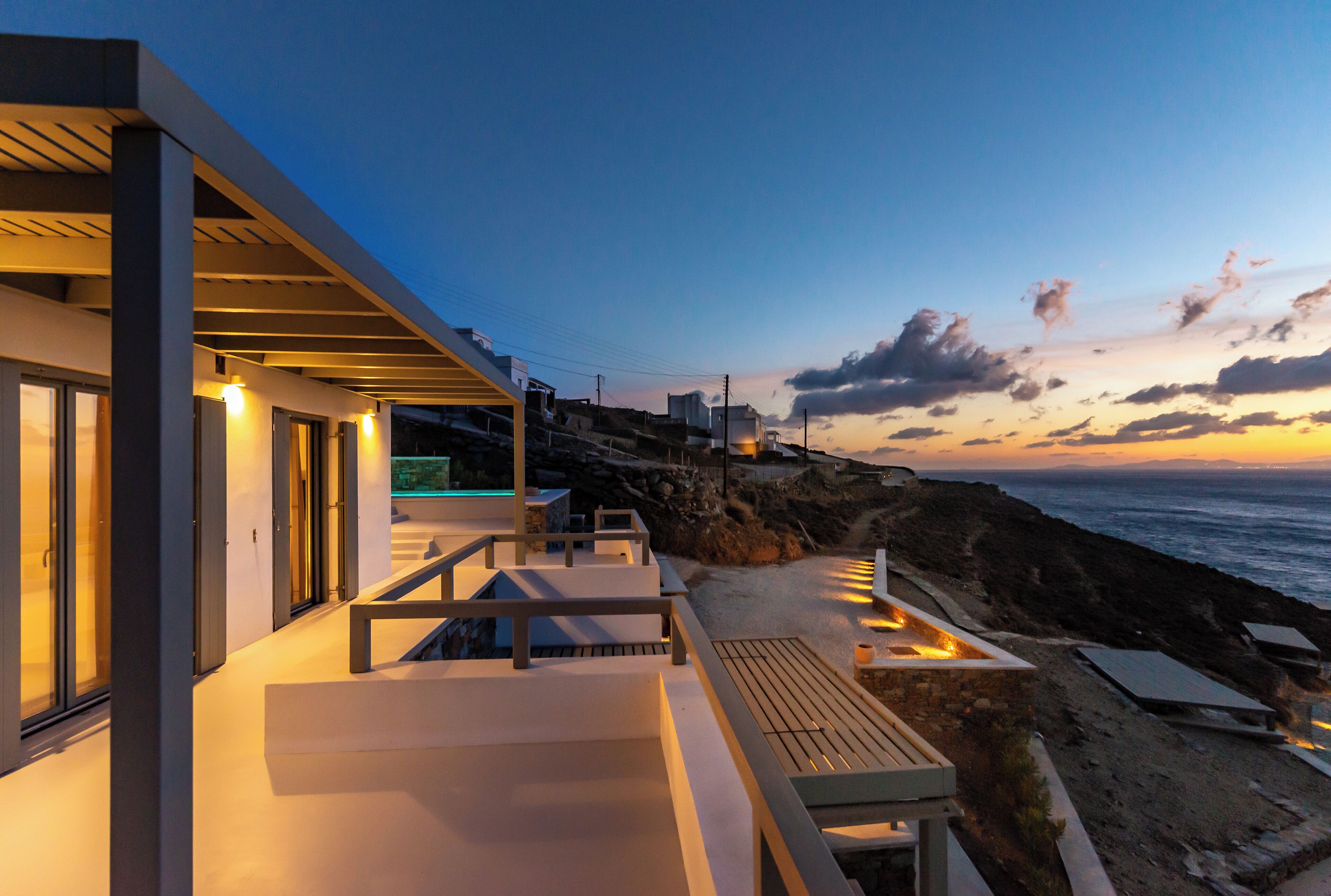 A modern building with a balcony overlooking a rocky coastline at sunset.