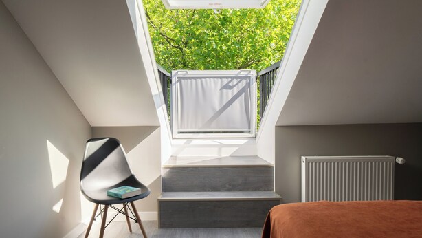 Quarto moderno com claraboia, uma cadeira, uma cama e um radiador.