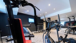 Academia com equipamentos de cardio, aparelhos de musculação e uma tela de televisão.
