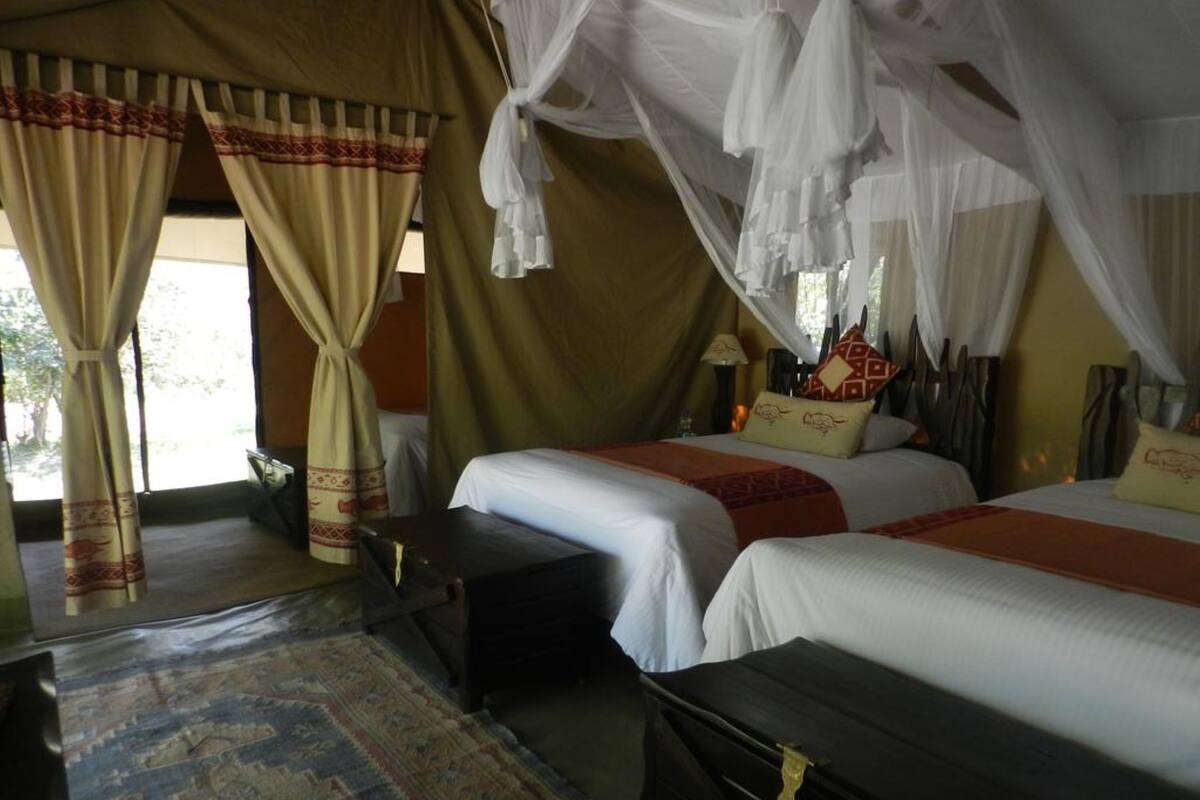 Quarto com duas camas, um baú de madeira, uma mesinha e um tapete estampado.