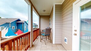 Un balcon fermé doté d’une balustrade en bois, une petite table avec des chaises et une vue sur les maisons voisines.