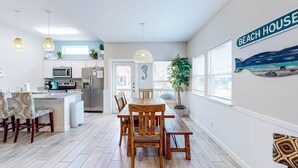 Une cuisine moderne avec des meubles blancs, un réfrigérateur en acier inoxydable et un coin repas comprenant une table et des chaises en bois.